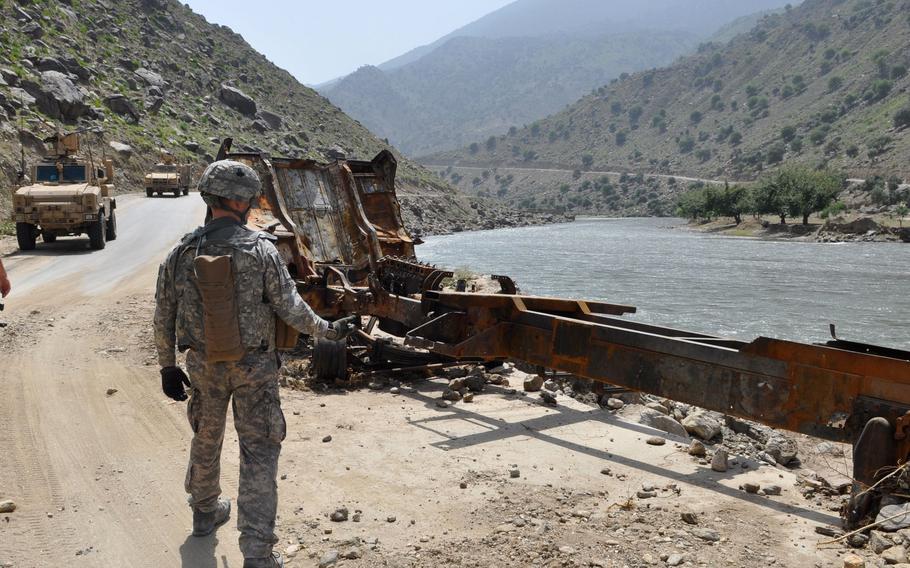 A soldier walks past the burned out shell of a supply truck that was attacked along the Pech River Valley road right outside the abandoned Tarale police station.