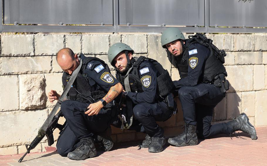 Israeli forces take cover on the side of a street in Ashkelon, Israel, as sirens wail while barrages of rockets are fired from the Gaza Strip into Israel on Saturday, Oct. 7, 2023.