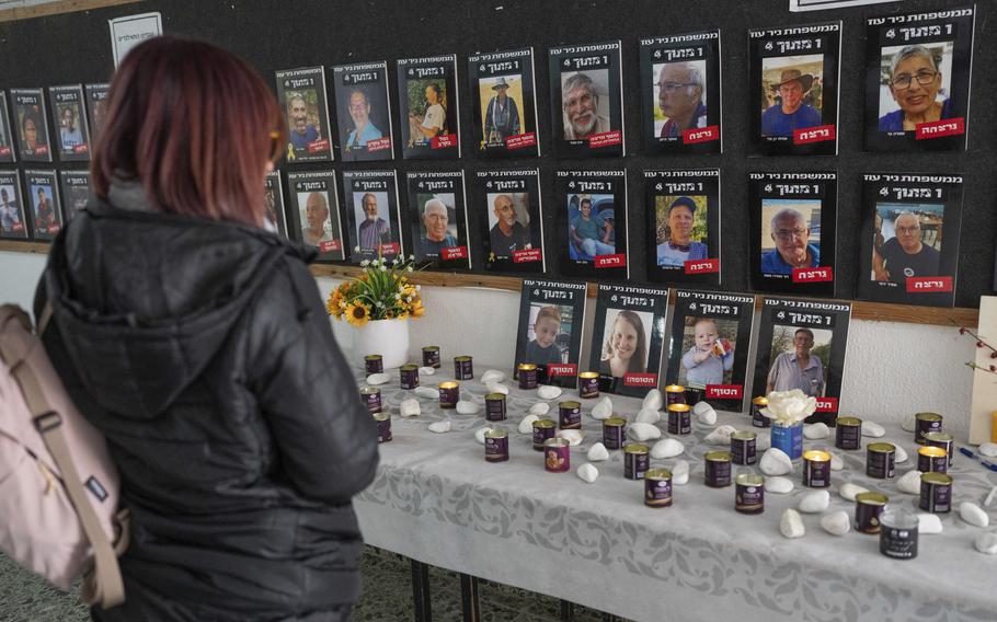 A woman with her back to the camera looks at a wall of photos of Israeli hostages above a table of candles.