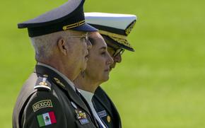 Mexican President Claudia Sheinbaum stands between two military officials to observe troops.