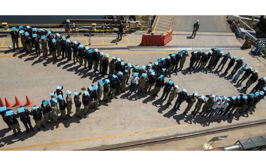 Sailors assigned to the amphibious assault ship USS Wasp (LHD 1) pose for a photo on a pier at BAE Systems Shipyard, April 29, 2022. Sailors stood in the shape a ribbon while holding teal paper to show support for sexual assault victims.