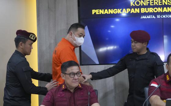 Chinese fugitive identified only by his initial LQ wears a mask escorted by Immigration officers during a news conference in Jakarta, Indonesia, Thursday, Oct. 10, 2024. (AP Photo/Tatan Syuflana)