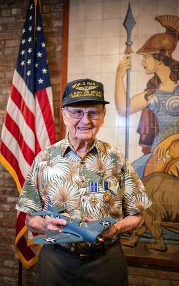 Richard E. “Dick” Miralles poses for a photo wearing his Distinguished Flying Cross and Air Medal and holding a replica of the Scout Bomber Douglas Dauntless dive-bomber at the California State Capitol Building in Sacramento, July 25, 2024. 