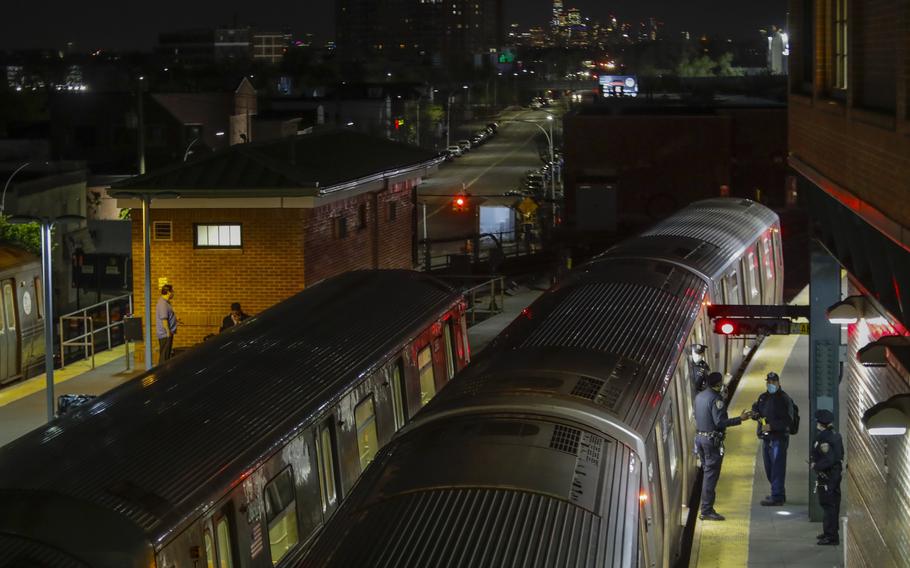 Police officers stand on a train platform beside a stopped commuter train.