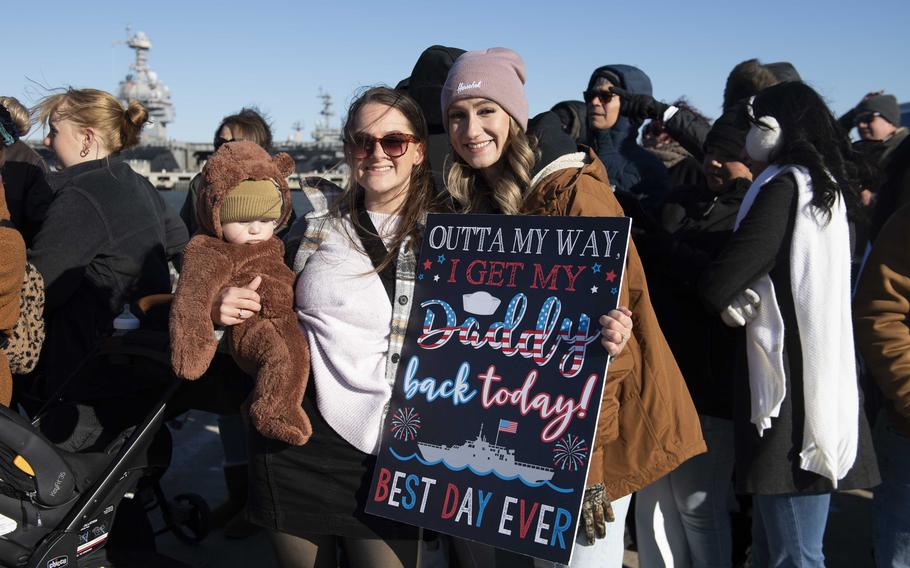 Family members of a sailor aboard the USS New York carry a sign that says “Outta My Way I get my Daddy back today!”