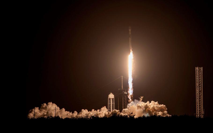 A rocket blasts off from a launchpad at night.