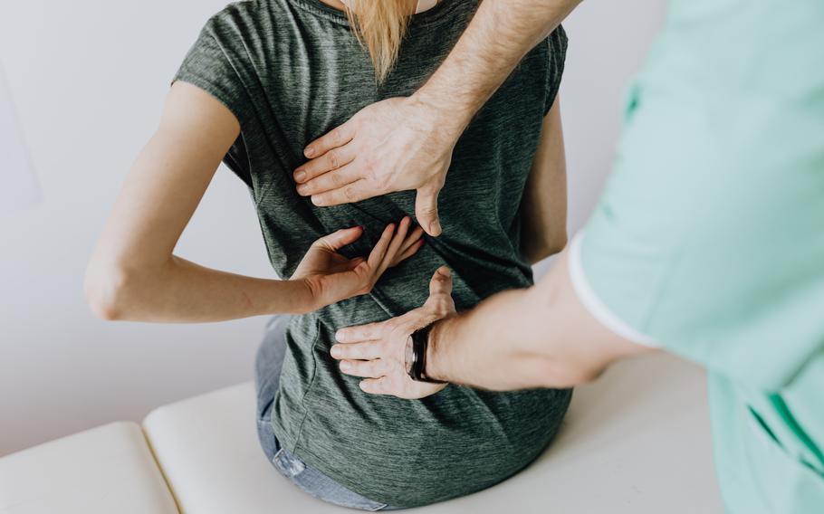 A woman points to pain areas in her back as a doctor checks.