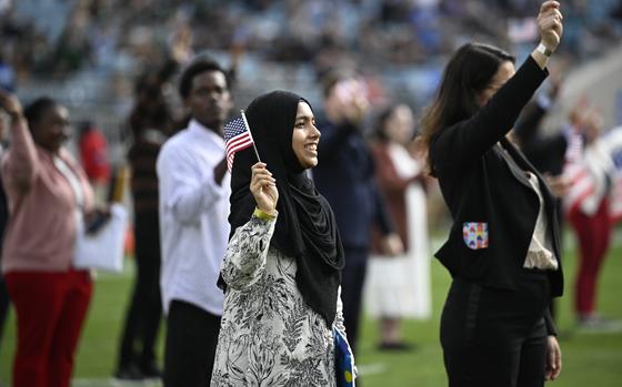 People stand in a football field, smiling and waving small American flags.