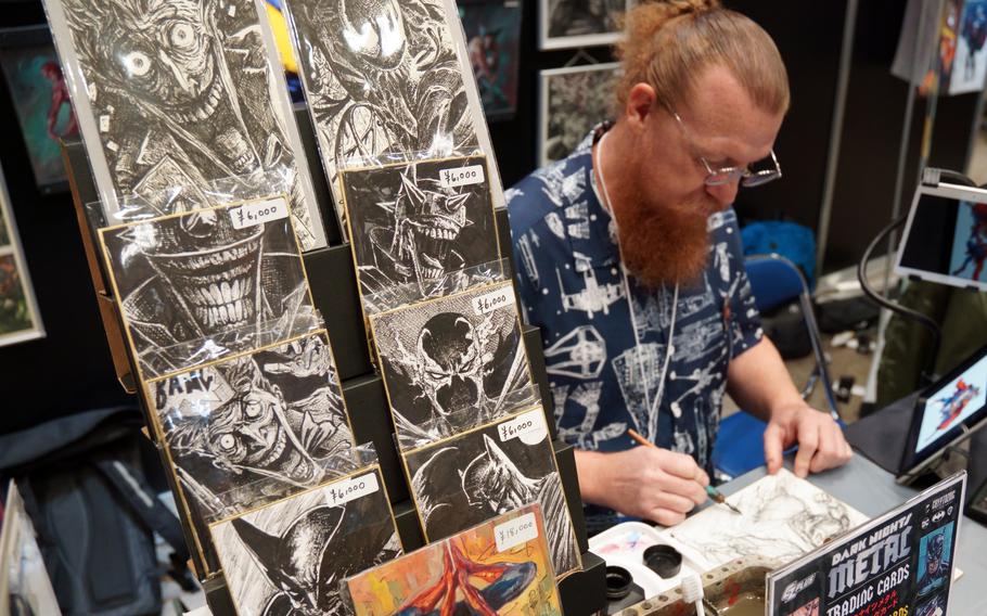 A man wearing a shirt decorated with star ships sketches in a notebook at a table.