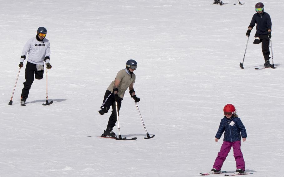 Three war veterans with amputated legs ski down a snowy slope using specialized equipment.