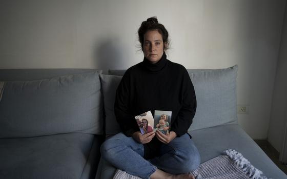 Yifat Zailer shows photos of her cousin, Shiri Bibas, center, her husband Yarden, left, and their sons Ariel, top right, and Kfir, who are being held hostage by Hamas militants in the Gaza Strip, as she poses for a portrait at home in Herziliyya, Israel, on Wednesday, Jan. 15, 2025. (AP Photo/Maya Alleruzzo)