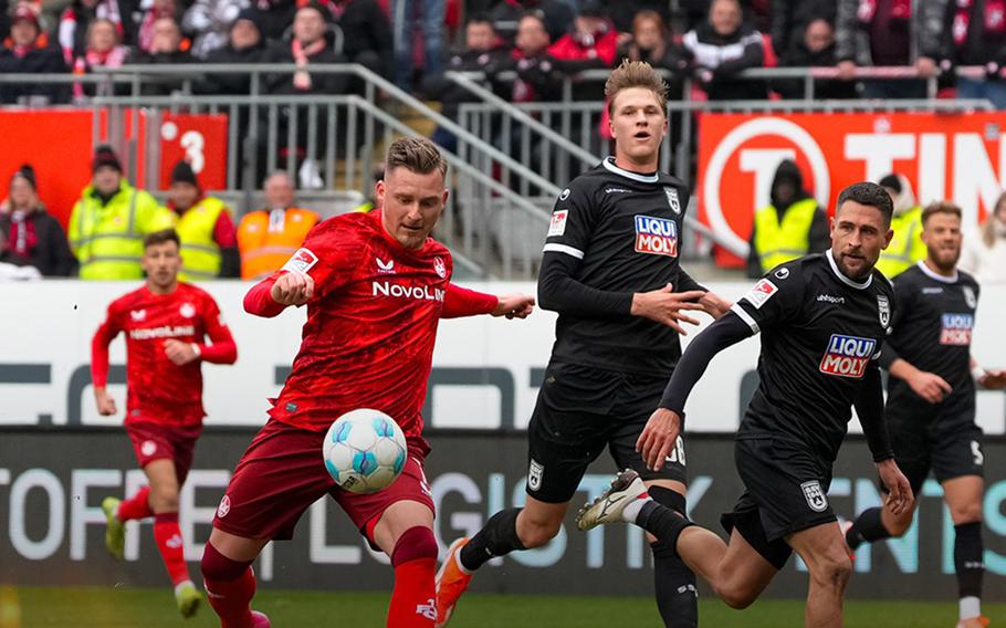 Two soccer players in red uniforms on the left, three in black on the right.