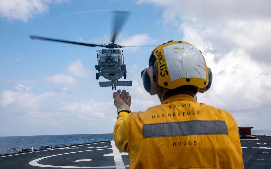 A sailor guides an Australian MH-60R Seahawk onto the guided-missile destroyer USS Benfold.