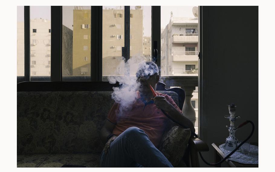 Mohammad Sabbah, who left Gaza with his wife and four children, smokes in his Cairo apartment. Rent in Egypt is expensive, he says — landlords “see us like a bag of money.” 