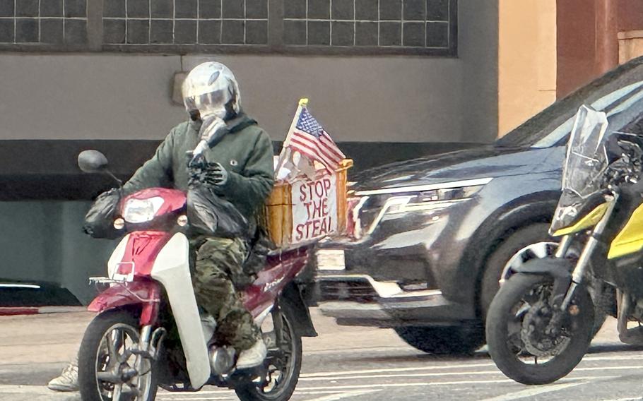 A person rides a motorcycle with an American flag and basket that says Stop the Steal.