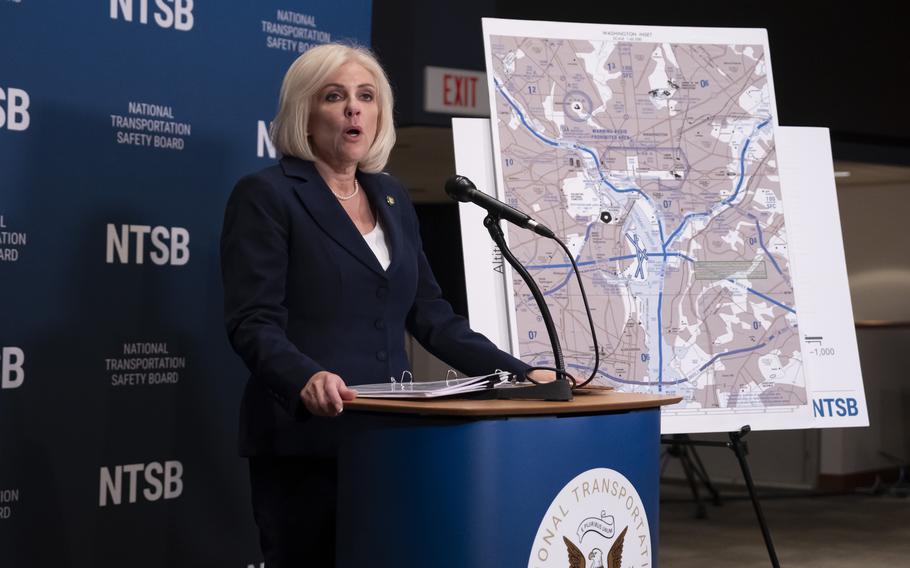 A woman in a dark suit stands at a podium and speaks into a microphone next to a large map sitting on an easel.