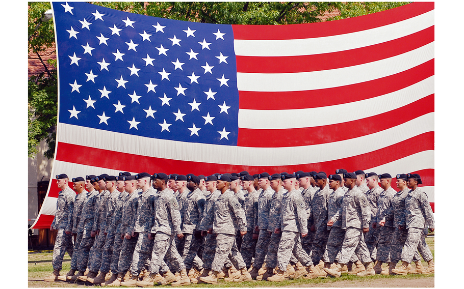 A formation of soldiers march in front of a large U.S. flag.