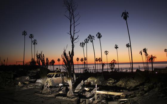 A sunset with water and burned trees and a vehicle in the foreground.