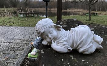 A baby statue sits in a garden bed in front of a small pond 