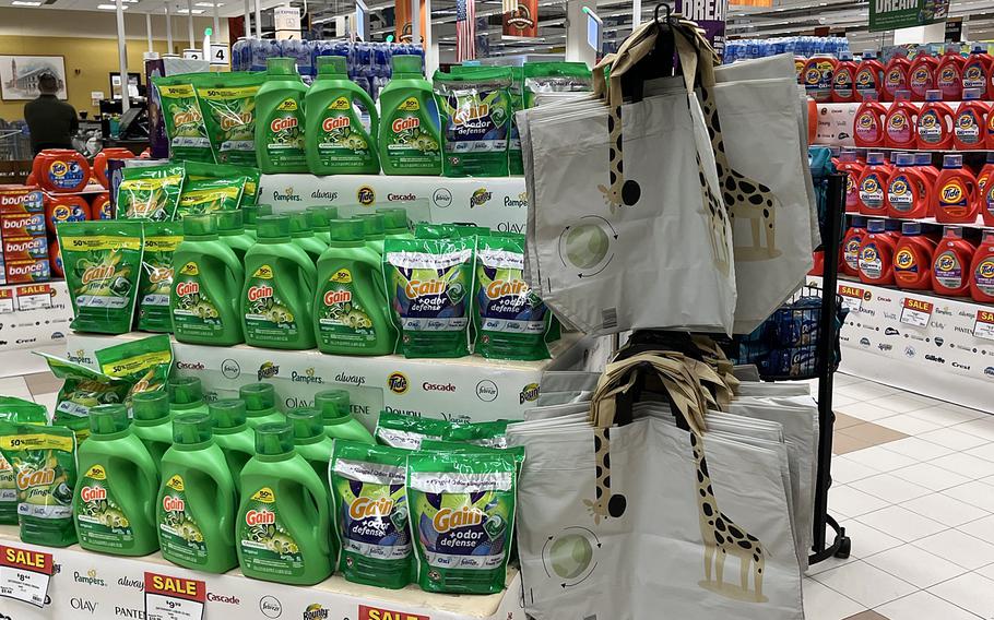 Reusable bags hang next to a grocery display of laundry detergent.