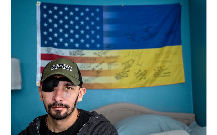 Giovanni Roman, a Marine Corps veteran, sits in his room at home in Orange County in front of a flag that is signed by Ukrainians he fought with while volunteering to serve on the front lines in the war against Russia, on April  25, 2023. Roman was badly injured when the vehicle he was traveling in was hit by a rocket, smashing his face and resulting in his losing an eye. Roman, now back at home in Orange County, is recovering from his injuries. 