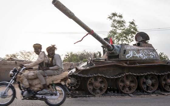 Soldiers from the paramilitary Rapid Support Forces ride by a destroyed tank belonging to the Sudanese Armed Forces in El Geneina, the capital of West Darfur, Sudan. MUST CREDIT: Diana Zeyneb Alhindawi for The Washington Post