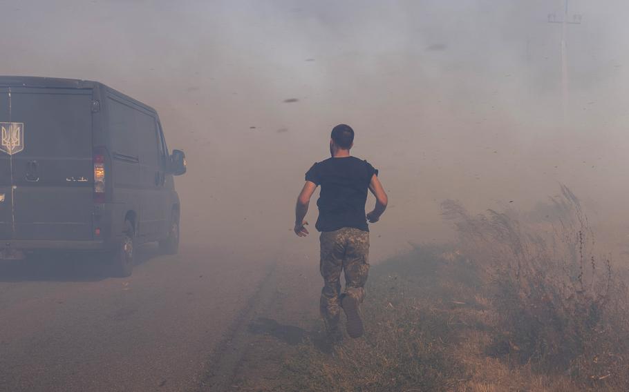 A Ukrainian serviceman runs to help farmers extinguish a burning field