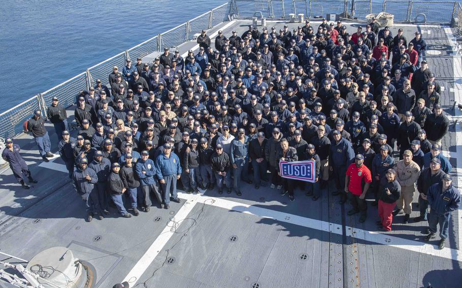 Comedian Jo Koy and sailors posing for a photo with the USO flag aboard the USS Shoup