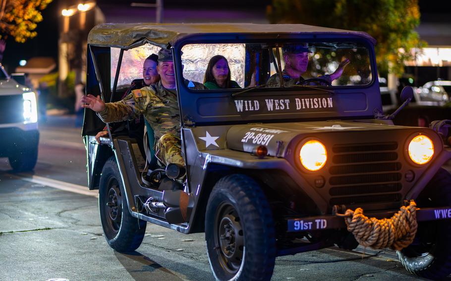 Soldiers and their wives ride in a historic jeep during a Christmas parade.