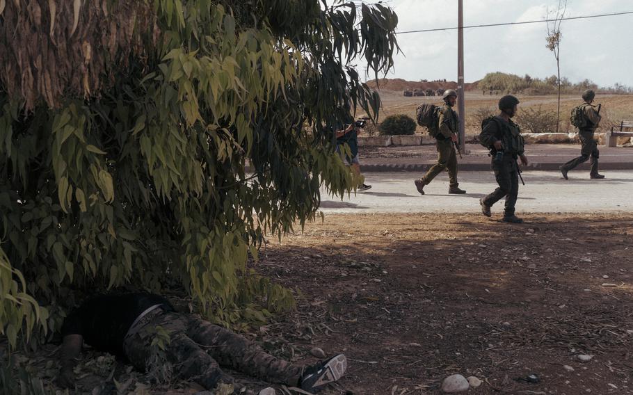 Israeli soldiers walk past the dead body of a militant in Kfar Azza, Israel, on Tuesday, three days after Hamas attacked the town.