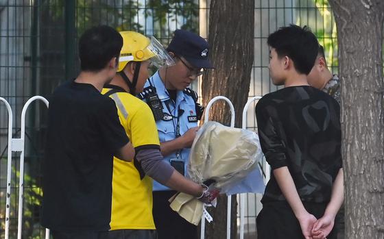 Police and security check a delivery rider (2nd L) who arrived with what appeared to be a bouquet of flowers at the entrance of the Japanese embassy in Beijing on Sept.19, 2024. China on September 19 expressed "regret and sadness" after a Japanese schoolboy who was stabbed in the southern city of Shenzhen died of his injuries. (Greg Baker/AFP/Getty Images/TNS)