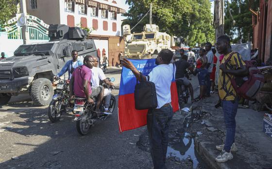 Armored police patrol past a man holding a Haitian flag in Port-au-Prince, Haiti, Friday, Sept. 20, 2024. (AP Photo/Odelyn Joseph)