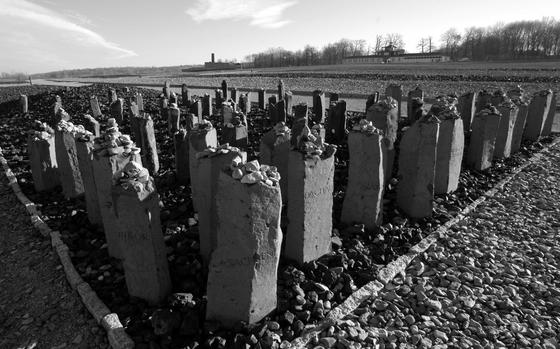 Stone markers stand in rows with smaller rocks on top and the names of concentration camp victims inscribed on the sides.