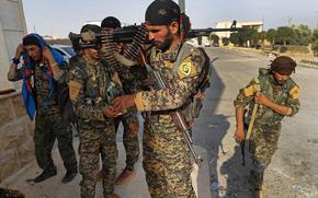 Five Kurdish fighters, some carrying rifles and one carrying a machine gun, in military fatigues.