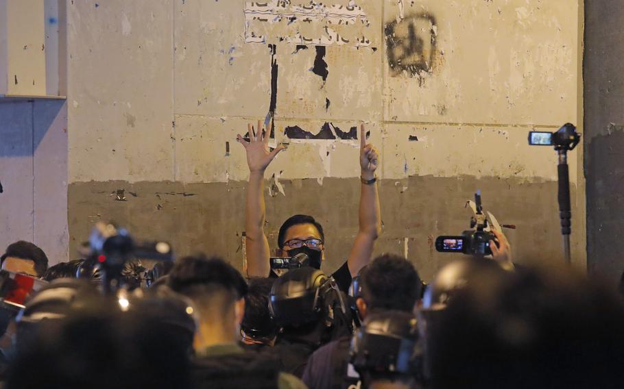 Then-lawmaker Lam Cheuk-ting gives a defiant gesture with raised hands while being surrounded by riot police and the media.