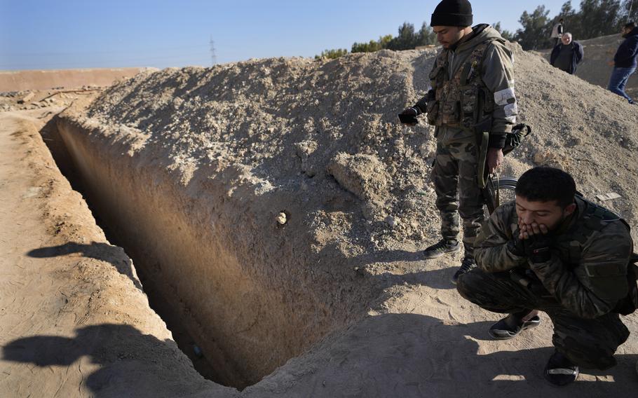 Syrian fighters from a rebel group stand over a ditch identified as a mass grave.