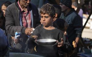 A Palestinian child in a refugee camp carries a bowl while waiting for food distribution.