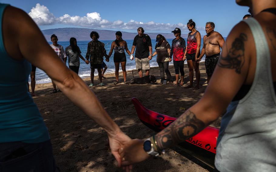 Members of the Lahaina Canoe Club hold hands in prayer before paddling out from Hanakaoʻo Beach in honor of Carole Hartley. 