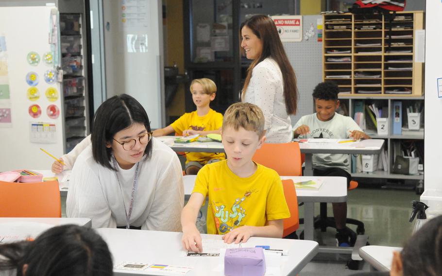 A teacher bends/crouches next to a boy in a yellow shirt.