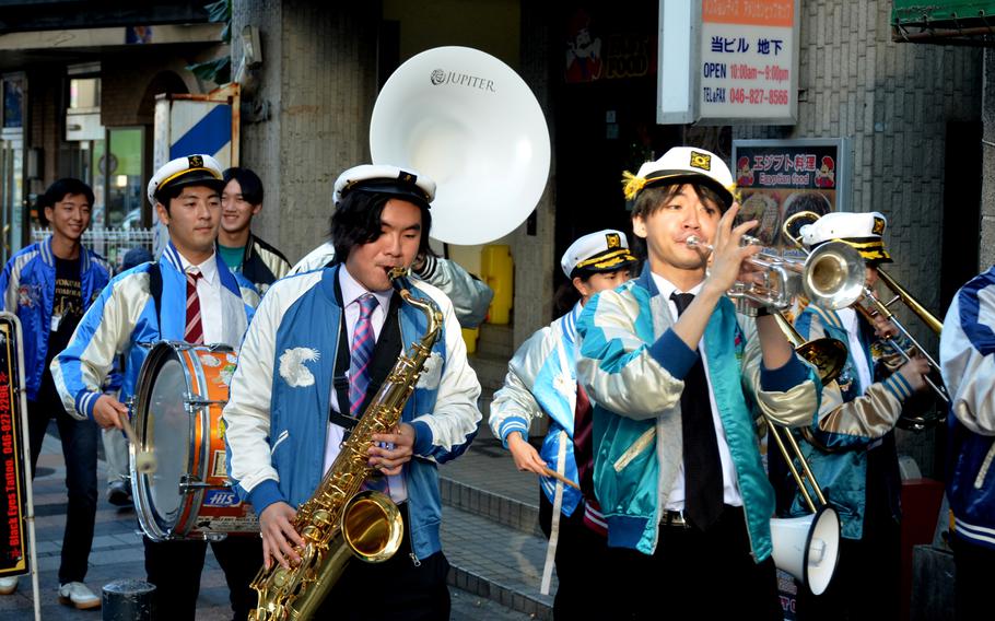 Japanese college students play instruments as they walk down a street.