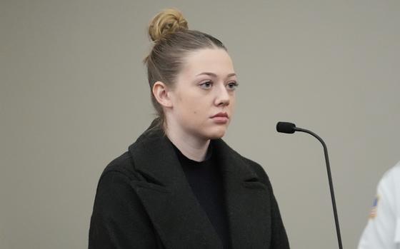 A young woman with her hair pulled back in a bun rests before a microphone.