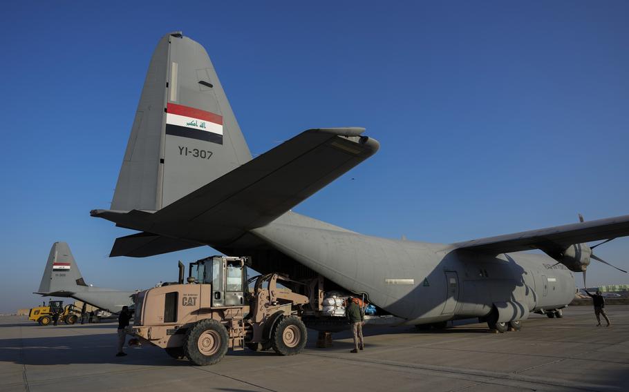 A plane is loaded with the help of a heavy equipment vehicle with blue skies overhead at a military base near Baghdad International Airport. 