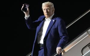 Donald Trump raises a hand with a phone while descending the steps from Air Force One.