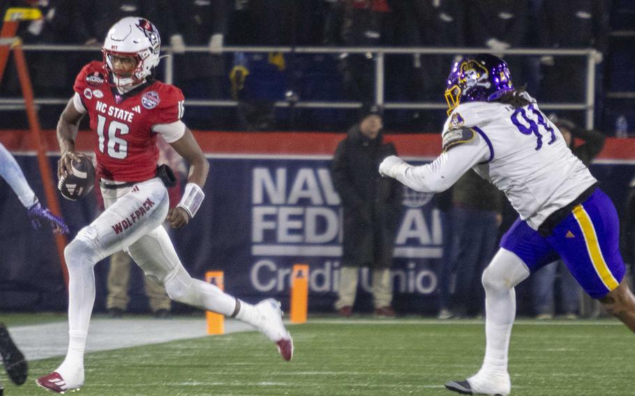 A football player in red holding the football runs past a football player in purple.