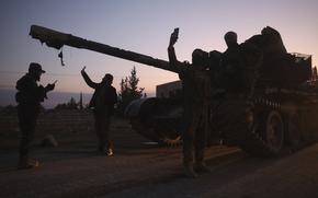 Militants silhouetted against a sunset stand next to a tank on a dirt road.