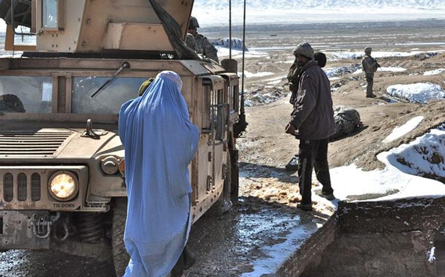 An Afghan family walks past a U.S. military Humvee stuck on a bridge where soldiers were changing a flat tire on Feb. 8, 2010. The soldiers were on a joint patrol with Afghan National Police in the Pashtun Zarghun district of Herat province in western Afghanistan.