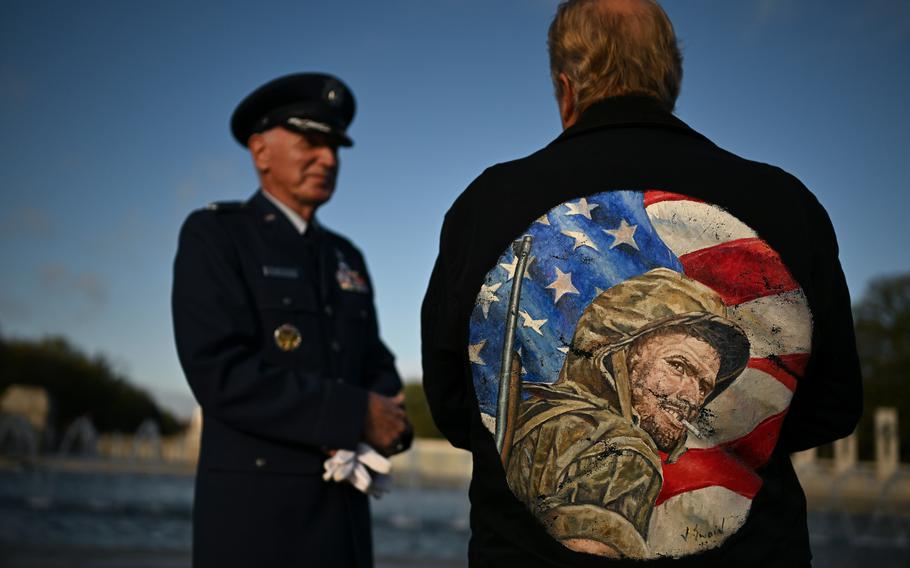 Jason Swain, wearing a jacket with a picture of a soldier in front of a U.S. flag, talks with retired Air Force Col. Sidney Wade.