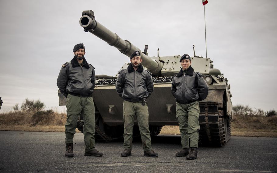 A three-man tank team stands in front of an Ariete tank.