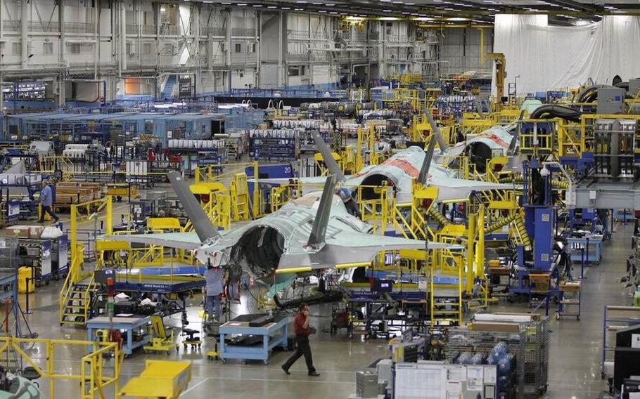 Workers in a warehouse put together three fighter jets.