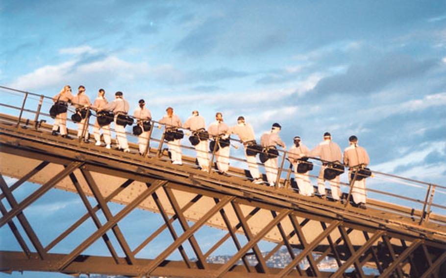 Climbers in “bridge suits” look out over the harbor in Sydney, Australia. A company called BridgeClimb guides small groups to the top of Sydney Harbour Bridge.